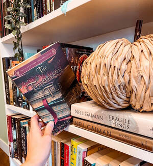 The Thirteenth Tale book is being pulled off a white shelf with a light brown paper weave pumpkin beside it.